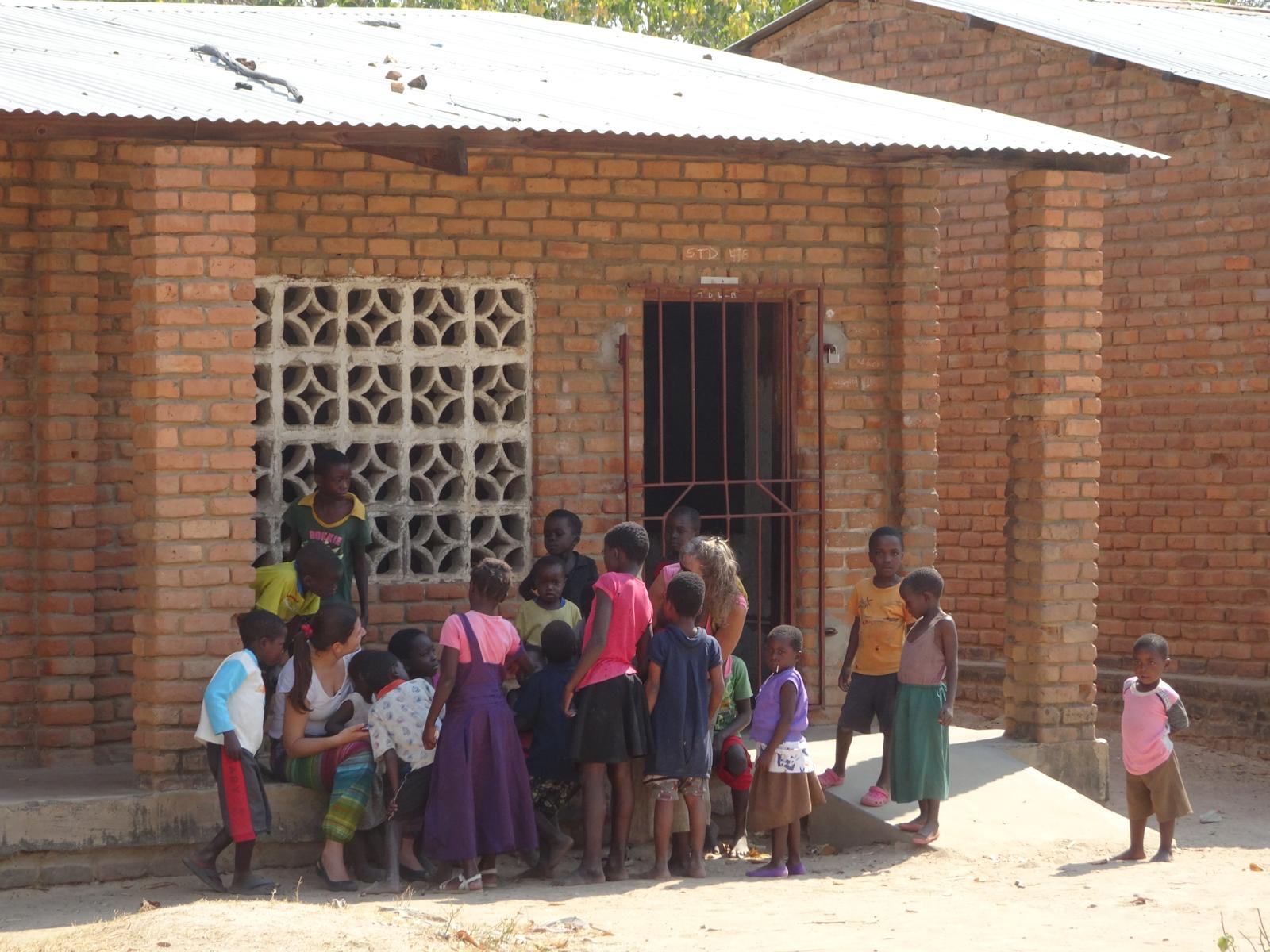 Dzieci i wolontariusze przy sali lekcyjnej szkoły podstawowej w Malawi