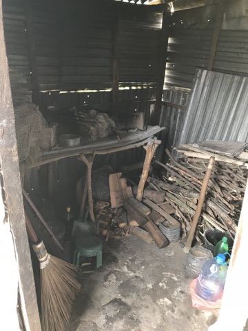 The inside of a corrugated iron hut, with firewood and household goods