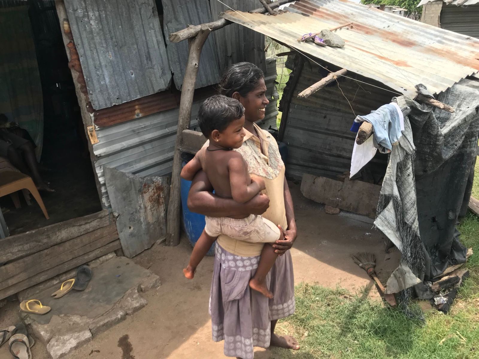 A mother holding her child in front of their corrugated iron home